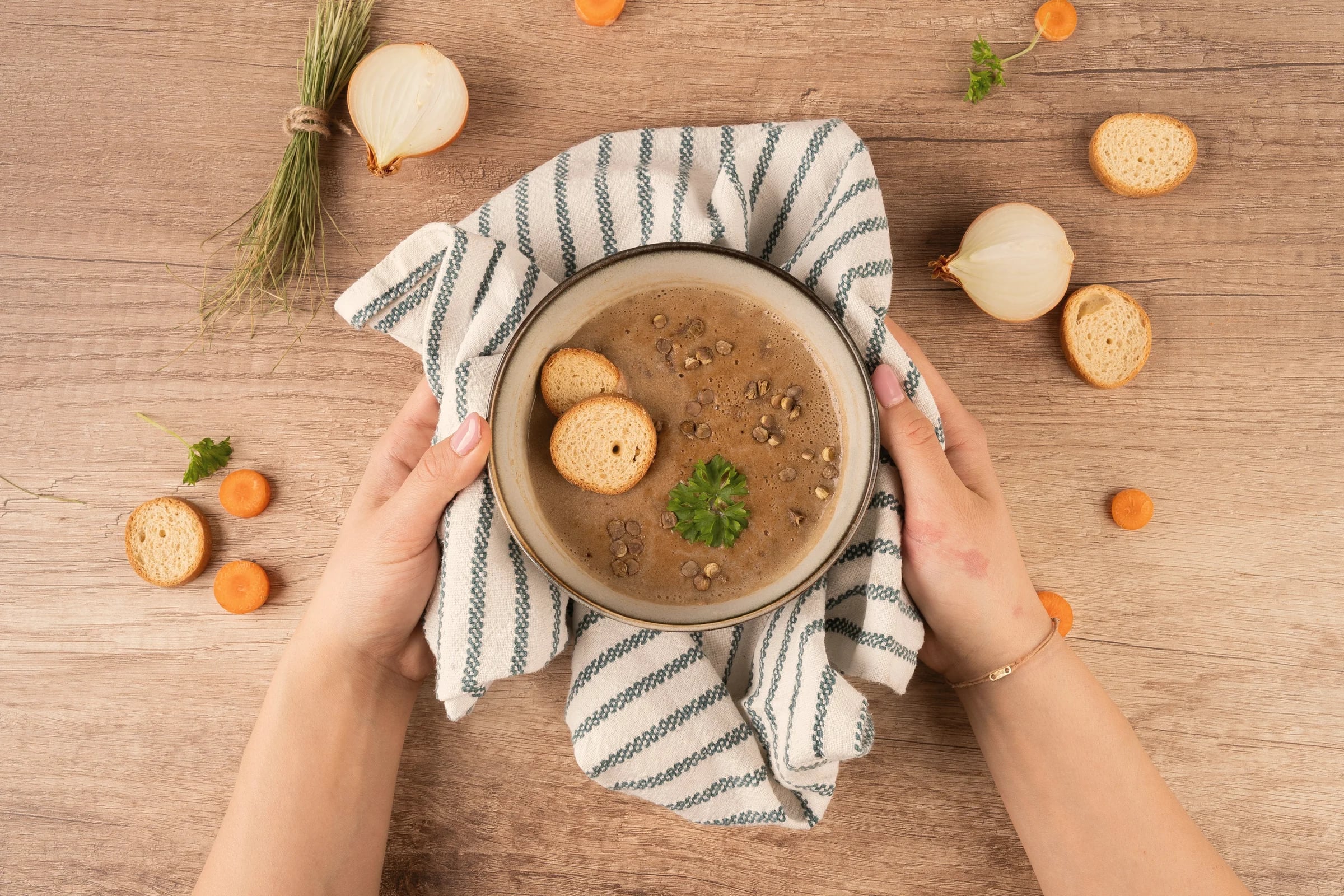 Hands holding a bowl of soup on a striped cloth