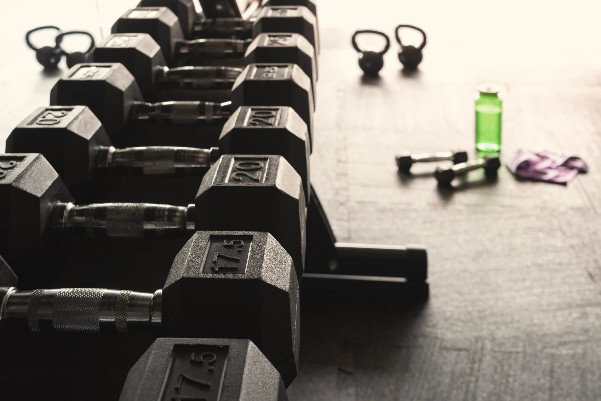 A rack of dumbbells with a water bottle on the gym floor
