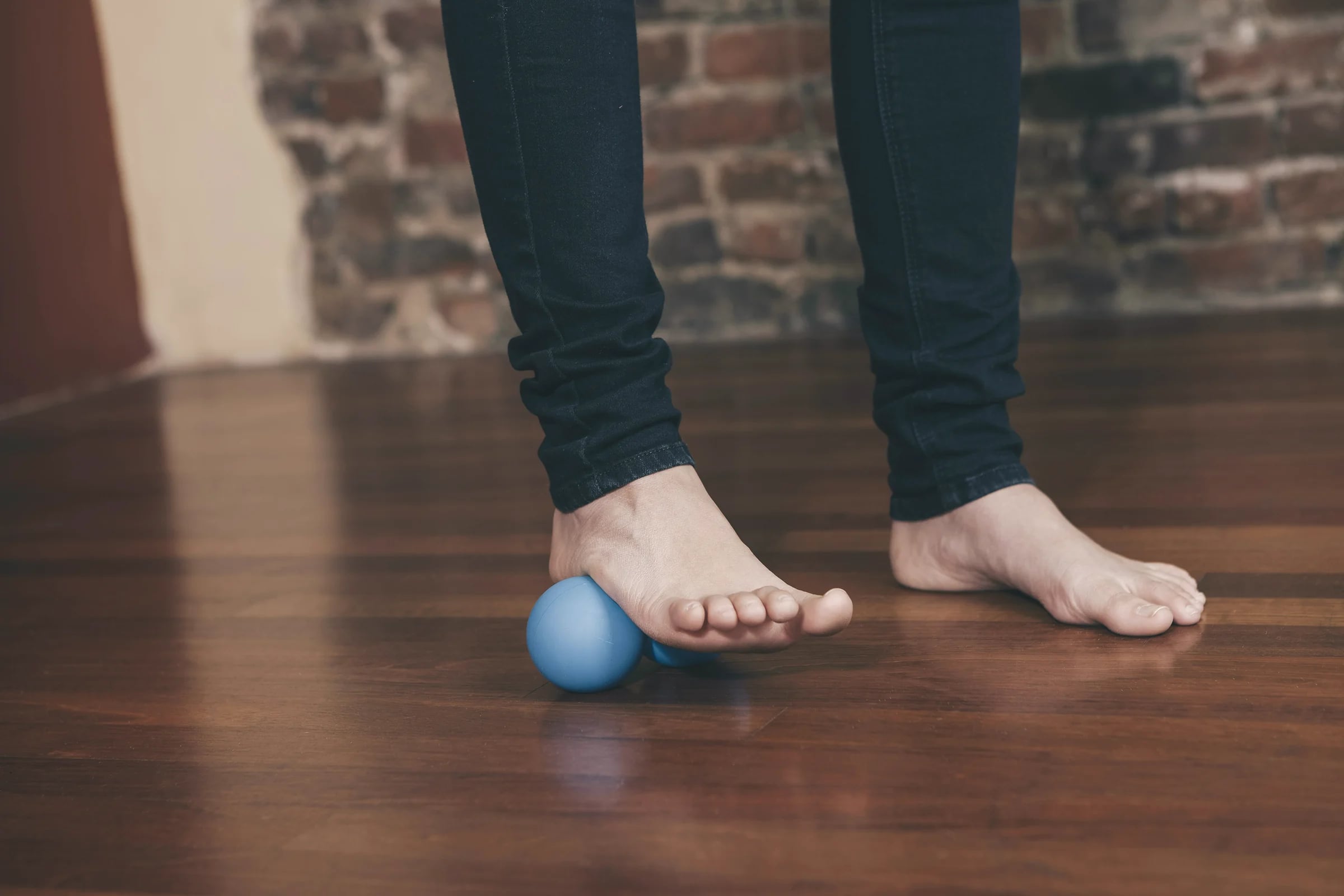 Bare feet rolling a massage ball on a wooden floor