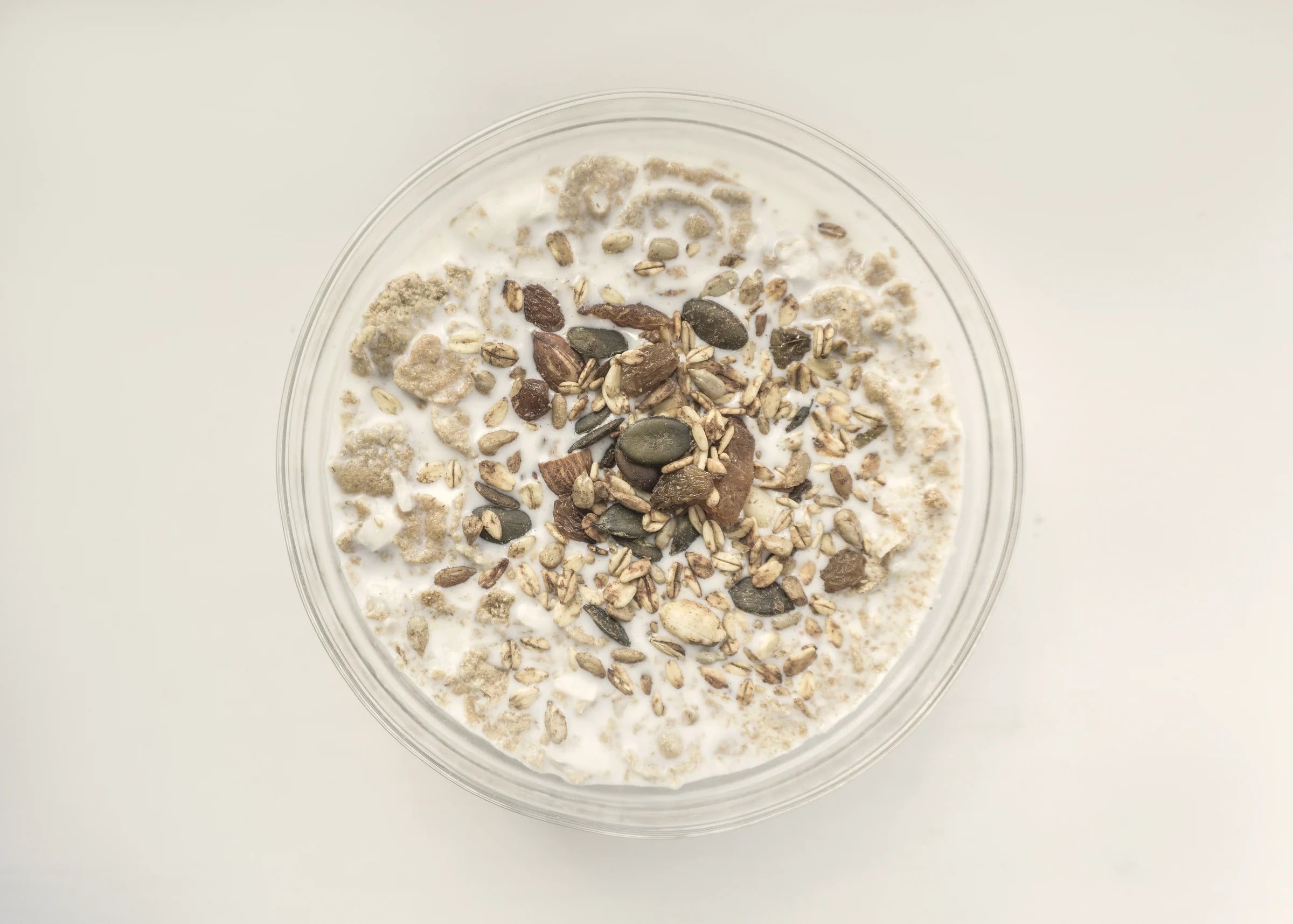 A glass bowl of muesli with milk on a white table