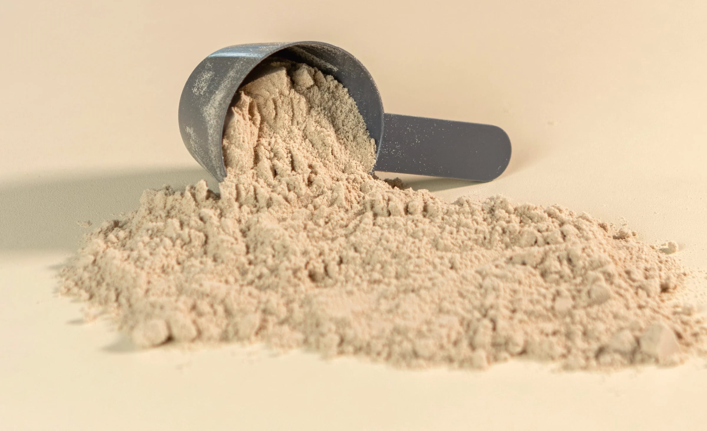 A scoop of protein powder tipped over on a pale cream surface