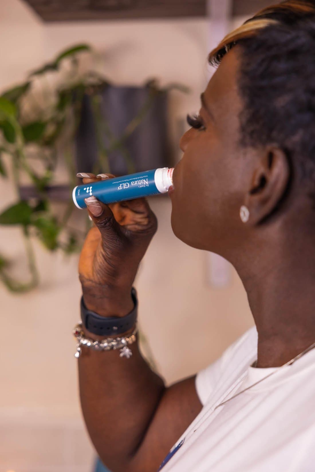 A woman takes her Natura daily drink stick beside a leafy plant.