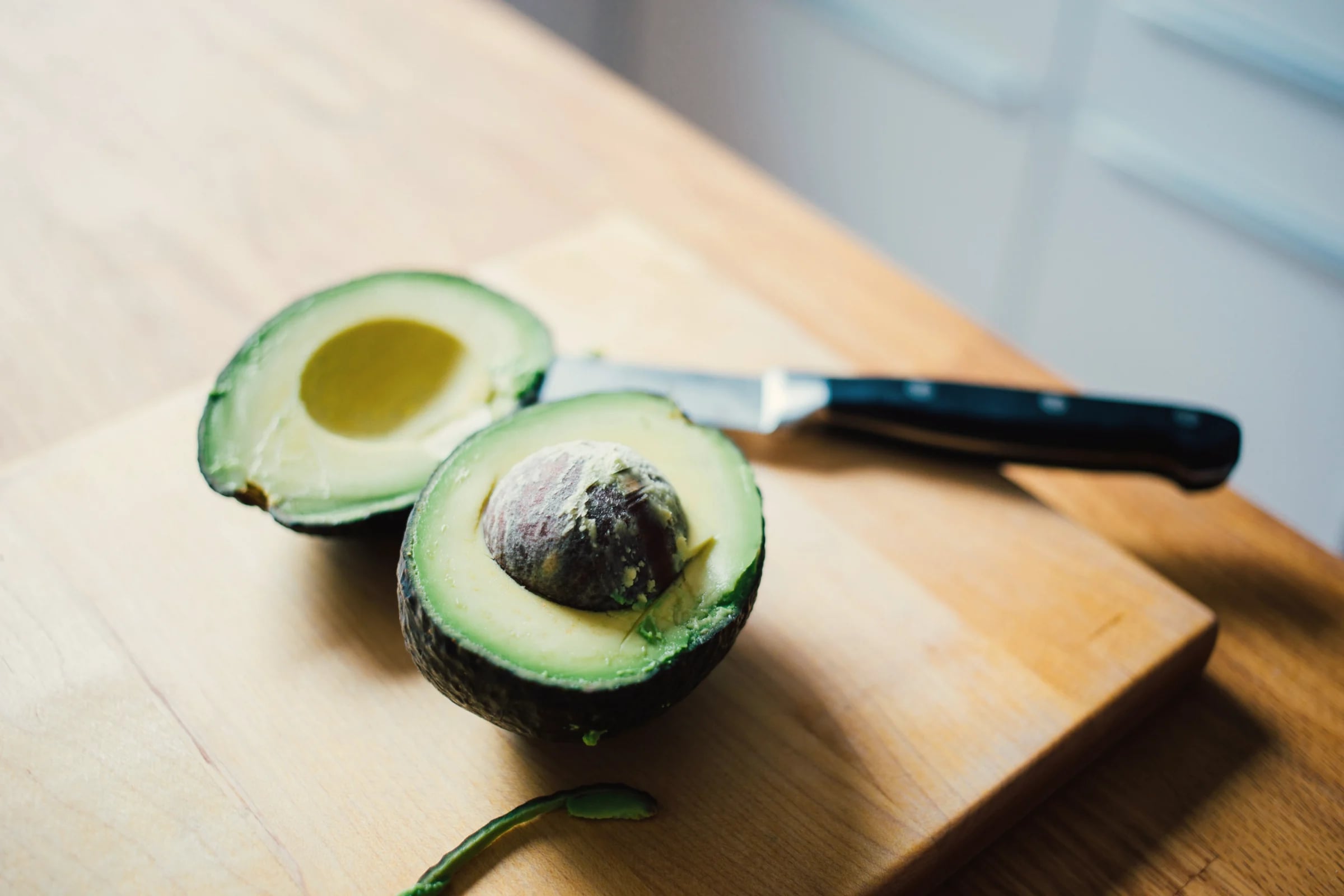 An avocado cut in half on a wooden chopping board